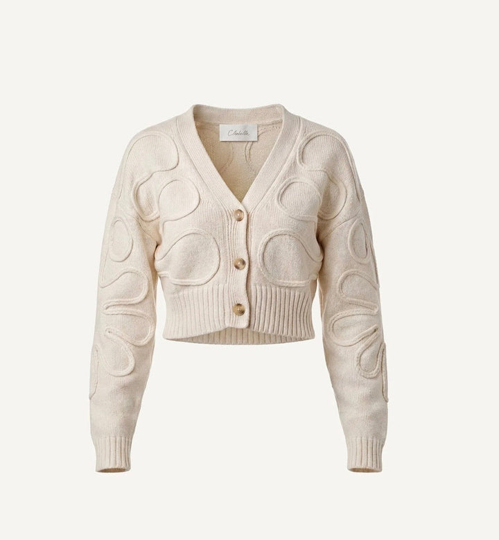 An off-white cropped cardigan sweater with a V-neck, three front buttons, and raised circular cable-knit patterns on the front and sleeves, shown against a solid off-white background.